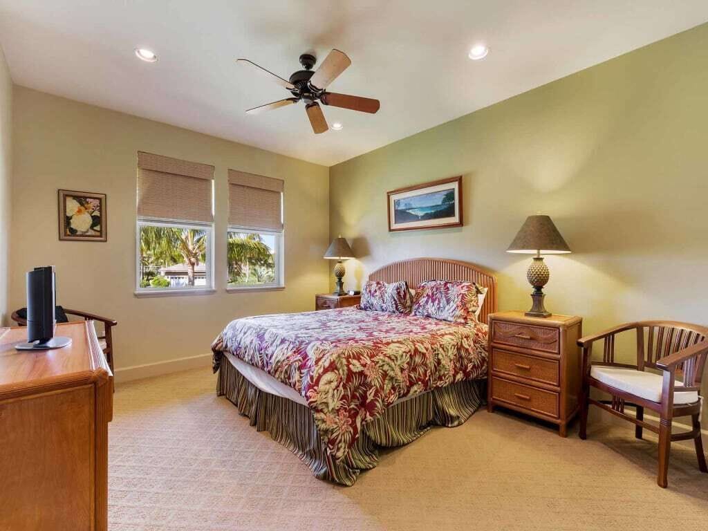 A bedroom with a bed, bedside tables, a chair, a desk, and a ceiling fan.