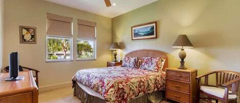 A bedroom with a bed, bedside tables, a chair, a desk, and a ceiling fan.