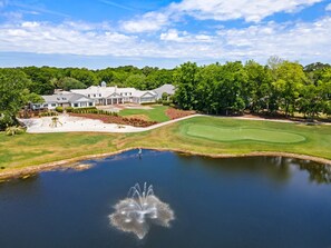 A golf course with a pond, a clubhouse, and a large house with a lawn.