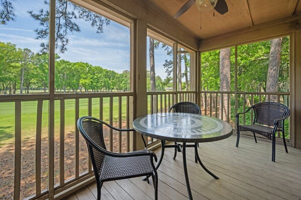 A covered outdoor seating area with a round table and four chairs, overlooking a grassy field and trees.