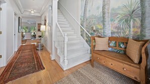 A spacious living area with a staircase, a large tropical mural, and a wooden bench with cushions.