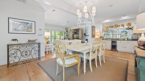 A spacious dining area with a large table, white chairs, and a chandelier.