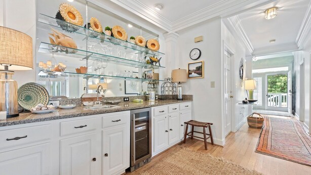 A modern kitchen with white cabinetry, a glass display shelf, and a wooden floor.
