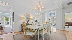 A dining area with a white table, four chairs, a chandelier, and a large mirror above the table.