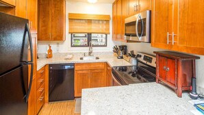 A kitchen with wooden cabinets, a stainless steel refrigerator, a microwave, and a stove. - Stylish Tropical Suite w/Bath+Kitchen Upgrades, WiFi, DVD, Lanai–Kaha Lani 113 (LIHUE)