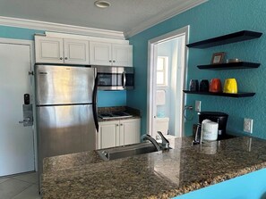 A kitchen with a stainless steel refrigerator, a microwave, and a stove. There are white cabinets and a granite countertop.