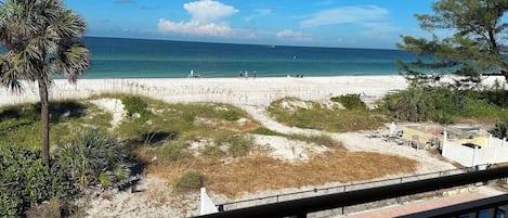 Strandudsigt fra en balkon med klar himmel, sandstrand og et par personer der går.