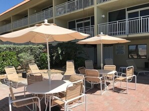 Un espace extérieur aménagé avec des tables et des chaises, des parasols, et un bâtiment avec des balcons en arrière-plan.
