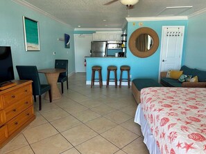 A hotel room with a bed, a TV, a dresser, a dining area with stools, and a kitchen area.