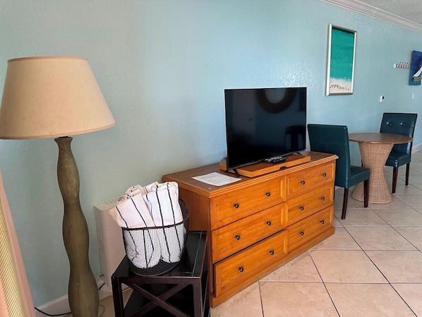 A room with a wooden dresser, a television on top, a lamp, and a wicker chair.