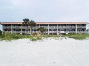Et motel ved stranden med en toetagers bygning, balkoner og en palme.