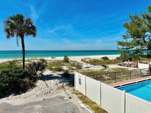 A beachfront property with a swimming pool, a sandy beach, and a clear view of the ocean.