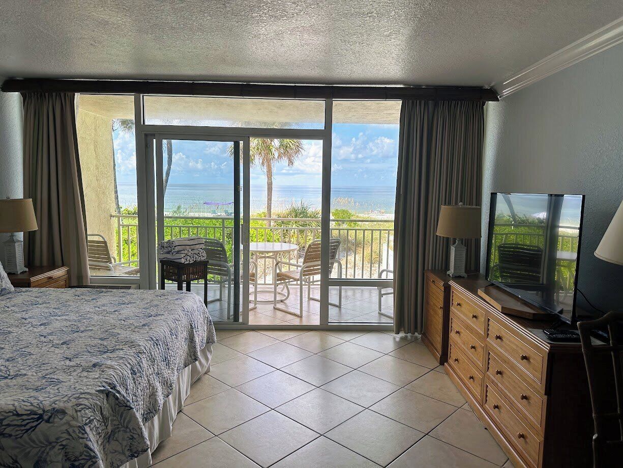 Une chambre d’hôtel avec un lit, une télévision, une commode en bois et un balcon équipé d’une table et de chaises.