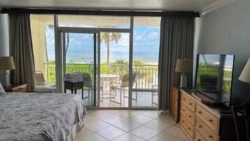 Une chambre d’hôtel avec un lit, une télévision, une commode en bois et un balcon équipé d’une table et de chaises.