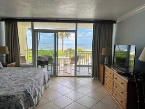 A hotel room with a bed, a TV, a wooden dresser, and a balcony with a table and chairs.