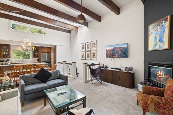 A spacious living room with a fireplace, a dining area, and a kitchen with wooden beams. - Riverside Condo with Mountain and Town views and updated furnishings. (Telluride)