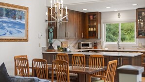 A modern kitchen with wooden cabinets, a central island, and a dining area with wooden chairs. - Riverside Condo with Mountain and Town views and updated furnishings. (Telluride)