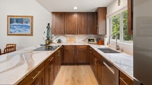 A modern kitchen with wooden cabinets, a marble countertop, and a built-in oven. - Riverside Condo with Mountain and Town views and updated furnishings. (Telluride)