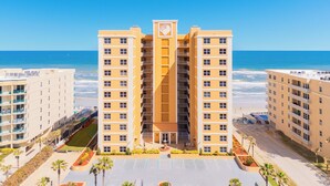 Un hotel de varios pisos con un atrio central, situado cerca de una playa bajo un cielo azul y despejado.