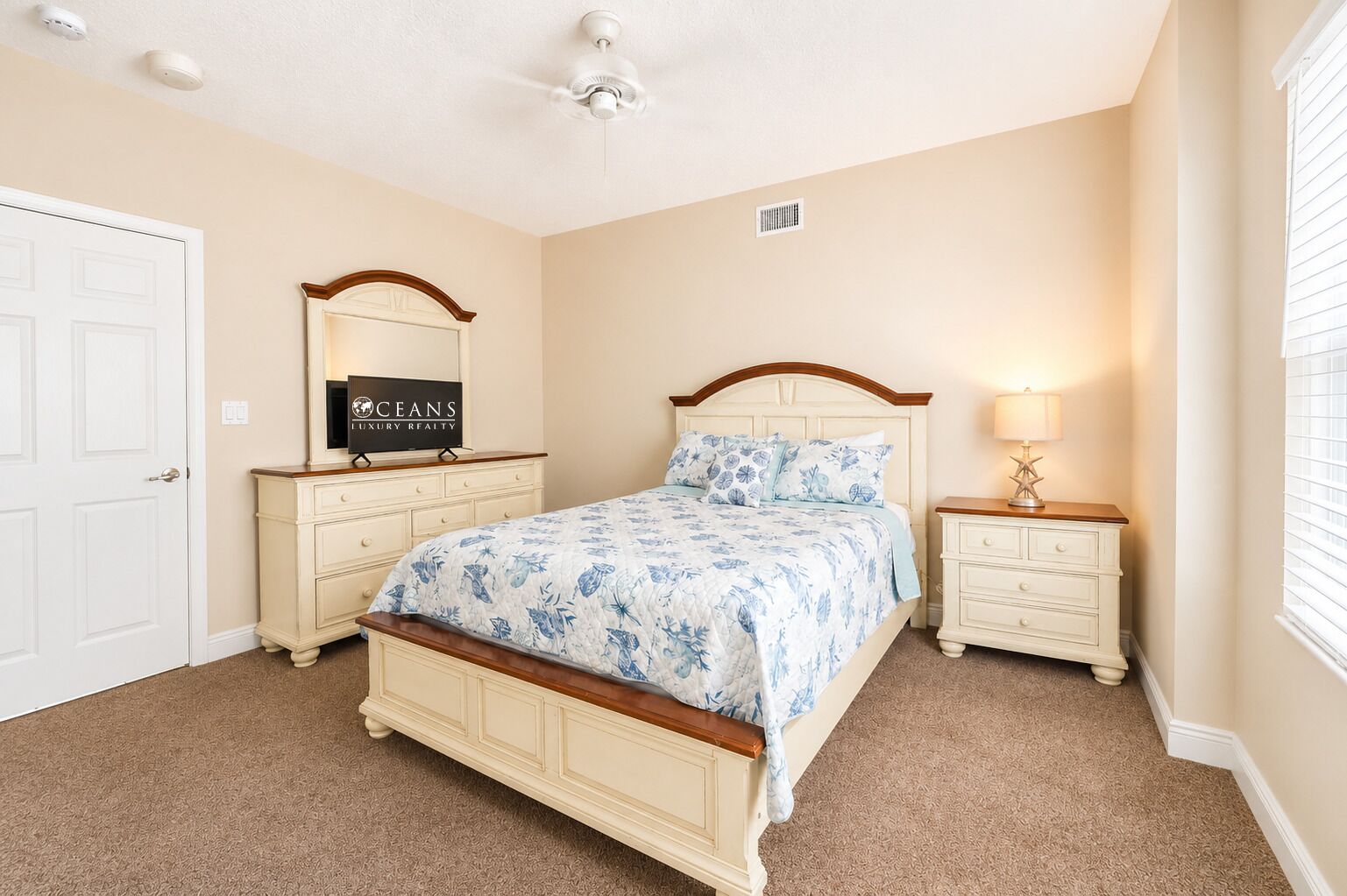 A bedroom with a bed, two nightstands, a dresser, a ceiling fan, and a door.