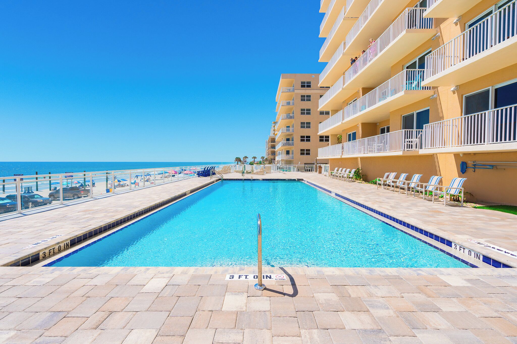 A swimming pool with a 3 ft 8 in depth marker, surrounded by a tiled deck and a building with balconies overlooking the pool.