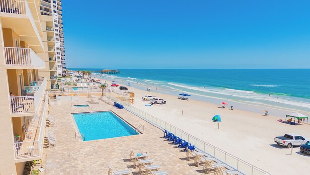 Un hotel con piscina, sillas de playa y vistas al océano.