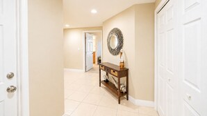 Un pasillo con paredes color beige, puertas blancas, una consola de madera con cestas y un espejo decorativo.