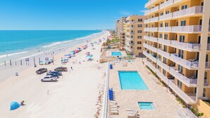 Un hotel frente a la playa con varios balcones, piscina y sombrillas.