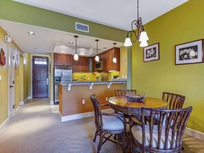 A dining area with a wooden table and chairs, a kitchen with wooden cabinets, and pendant lighting.