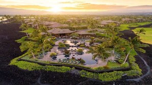 Un resort con varias edificaciones, un área de piscina central y palmeras circundantes.