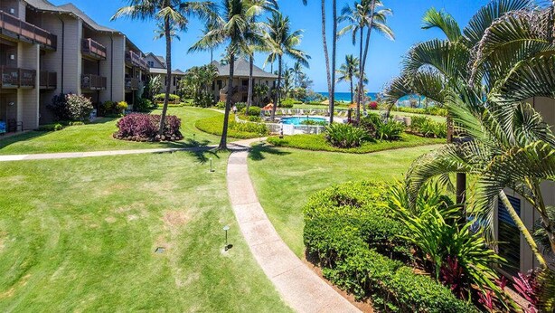 A hotel courtyard with a swimming pool, palm trees, and a clear blue sky. - Island Touches w/Modern Kitchen, Wood Floors, Lanai, Flat Screen, WiFi–Kaha Lani 203 (LIHUE)