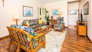 A living room with a sofa, chairs, a coffee table, and a TV stand. - Island Touches w/Modern Kitchen, Wood Floors, Lanai, Flat Screen, WiFi–Kaha Lani 203 (LIHUE)