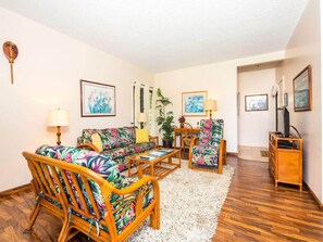 A living room with a sofa, chairs, a coffee table, and a TV stand. - Island Touches w/Modern Kitchen, Wood Floors, Lanai, Flat Screen, WiFi–Kaha Lani 203 (LIHUE)