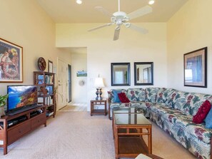 A living room with a television, sofa, coffee table, and ceiling fan.