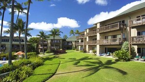 A hotel with multiple balconies, a well-maintained lawn, and palm trees.