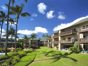 Hotel com várias varandas, área de piscina e palmeiras.