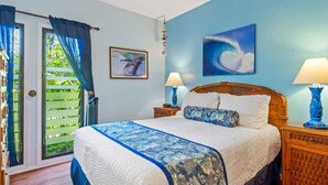A bedroom with a bed, two nightstands, a ceiling fan, a window with curtains, and a door. - Ground-Floor Ocean View W/Lanai–Kaha Lani #105 (LIHUE)