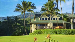 A large, two-story house with a green roof, surrounded by a well-maintained lawn and tall palm trees. - Ground-Floor Ocean View W/Lanai–Kaha Lani #105 (LIHUE)