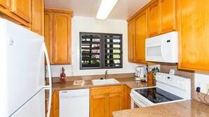 A kitchen with wooden cabinets, a white refrigerator, a microwave, a stove, and a dishwasher. - Ocean Suite Life Steps from Surf – Kaha Lani 120 (LIHUE)