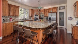 A spacious kitchen with wooden cabinets, a large island with bar stools, stainless steel appliances, and a view of the outdoors through a window. - Sierra Sky - Luxurious Retreat with Free Private Lake Access! (Arnold)