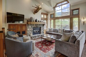 A spacious living room with a stone fireplace, a mounted deer head, and a large window offering a view of the outdoors. - 3BR/3.5BA Townhome Steps to Beaver Creek Village & Lifts (Beaver Creek)