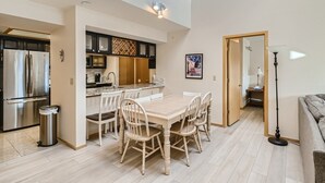 A modern kitchen with a stainless steel refrigerator, a dining area with a wooden table and chairs, and a living room with a sofa and a floor lamp. - Two Bedroom Plus Loft with Awesome Views of Lake Dillon (Frisco)