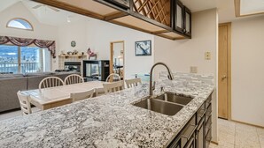 A modern kitchen with a granite countertop, stainless steel sink, and a dining area with a table and chairs. - Two Bedroom Plus Loft with Awesome Views of Lake Dillon (Frisco)
