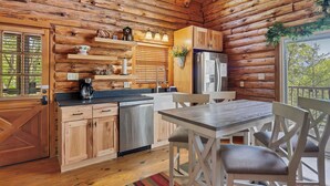 Eine Kücheneinrichtung in einer Blockhütte mit Holzausbau, einem Geschirrspüler, einem Kühlschrank und einem Esstisch mit Stühlen.