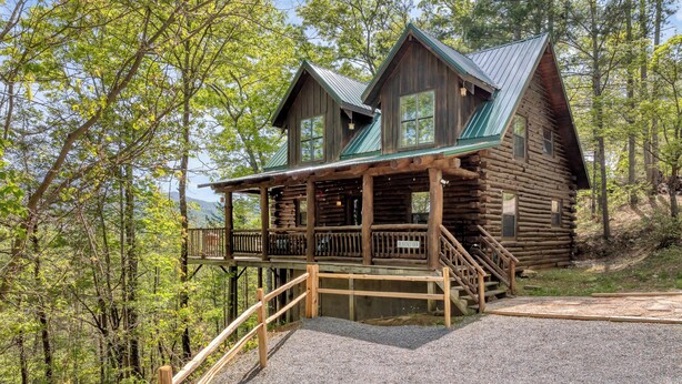Eine Blockhütte mit Veranda und einer Treppe, die zu ihr hinaufführt, umgeben von Bäumen.