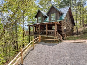 A log cabin with a porch and a staircase leading up to it, surrounded by trees.