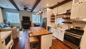 A modern kitchen with wooden flooring, white cabinetry, a central island with stools, a built-in oven, and a large window providing natural light. - HotTub, OutdoorShower, Renovated Barndominium, WiFi, Fireplace, Pet Friendly (Ferguson)
