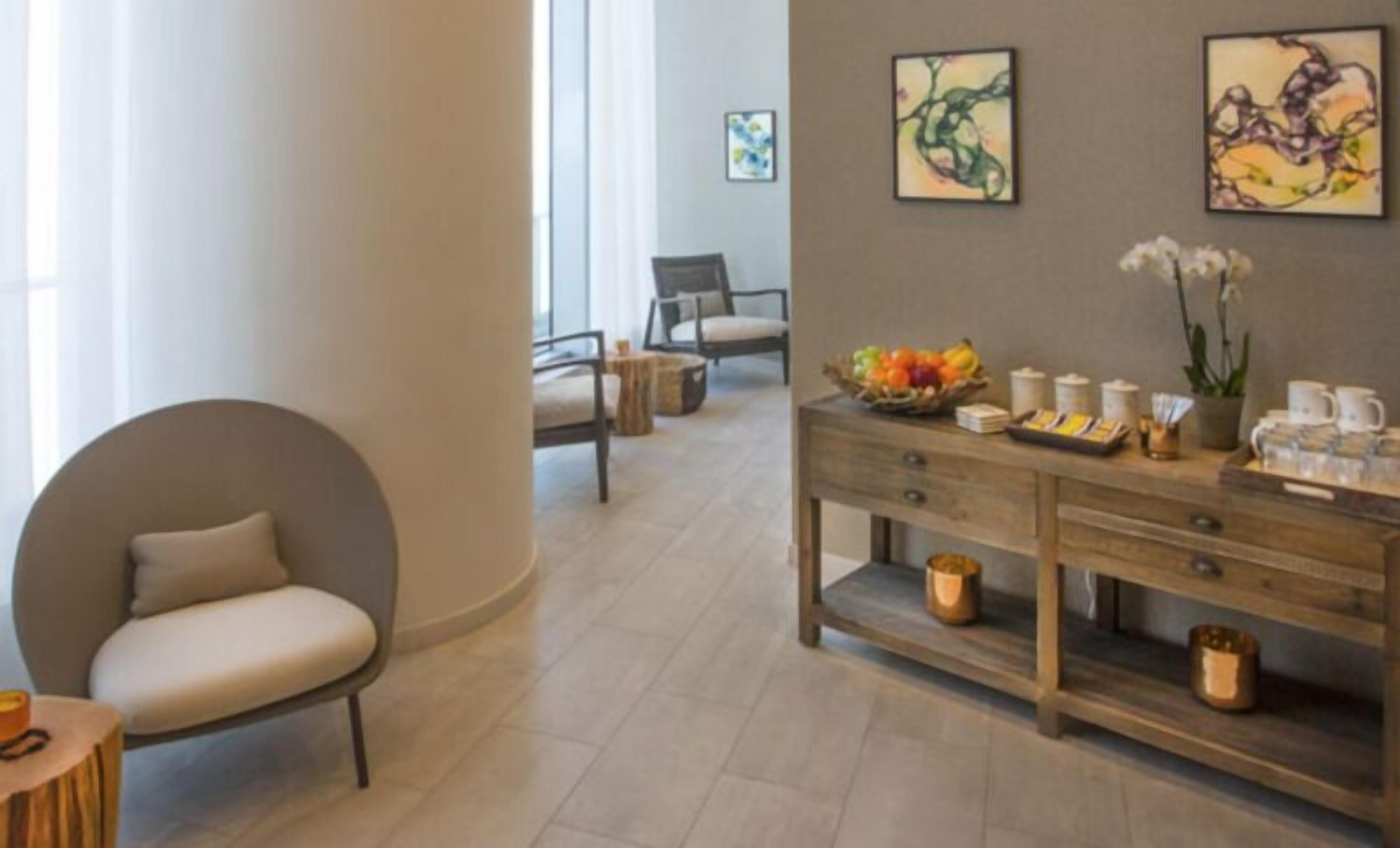 A modern hotel lobby with a round seating area, a wooden reception desk with amenities, and abstract art on the walls.