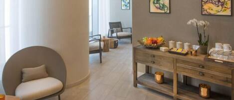 A modern hotel lobby with a round seating area, a wooden reception desk with amenities, and abstract art on the walls.