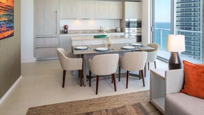 Una cocina moderna con armarios de madera clara, una mesa de comedor con sillas y vistas al océano a través de amplios ventanales.